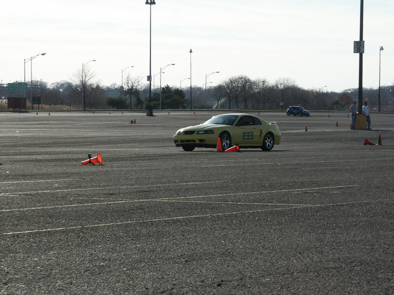 Yellow Ford Mustang with number 233 on the door, driving in a parking lot with cones