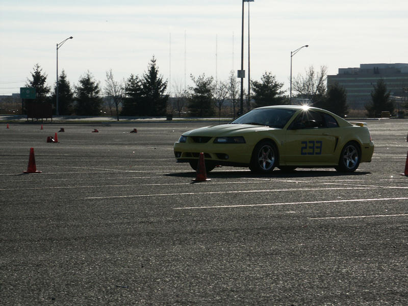 Yellow coupe with racing number 233 on the door, parked on asphalt with orange cones