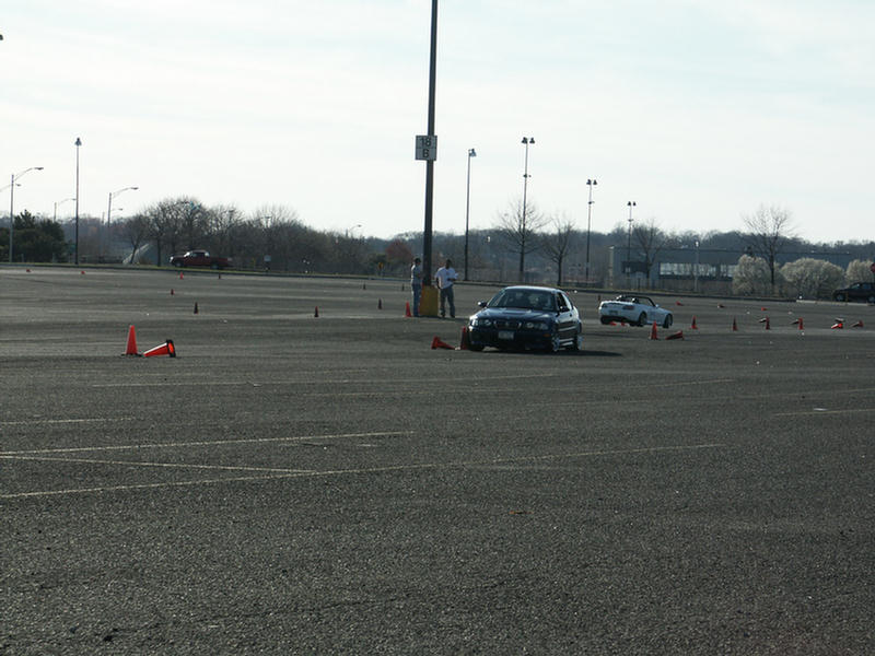 dark sedan and white convertible on a paved lot with cones
