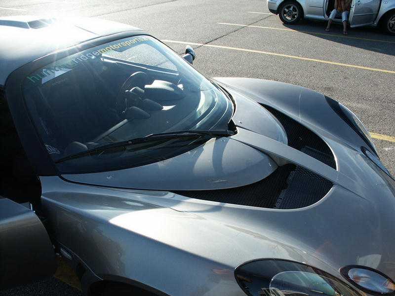 Silver Lotus Elise with a banner on the windshield. Another car is parked nearby