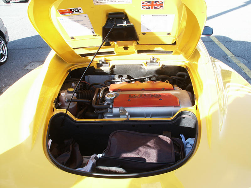 Yellow Lotus engine compartment with orange and red engine covers, open hood, and luggage in the trunk