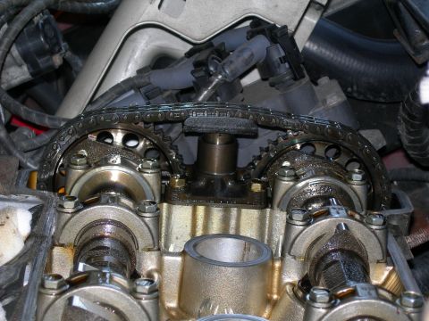 1992 Ford Taurus - Close-up of a dual-overhead-cam cylinder head with the valve cover removed, showing the twin cam sprockets, timing chain and a chain guide/…