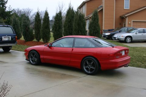 1993 Ford Probe - A red 1993 Ford Probe is parked on a wet driveway in front of a house.