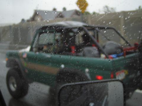 1985 Ford Bronco - Green SUV with roll cage driving in the rain.