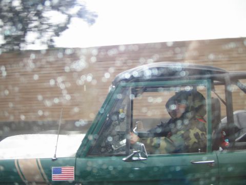 1985 Ford Bronco - Two individuals are seen inside a green SUV, with an American flag sticker on the exterior.