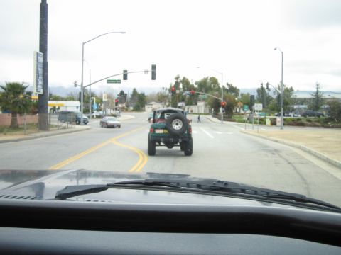 1985 Ford Bronco - A green Jeep Wrangler is seen from behind, driving on a street with traffic lights and other vehicles.