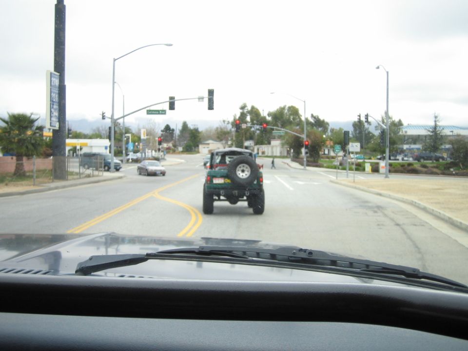Green SUV with rear spare tire seen through windshield at a red-light intersection