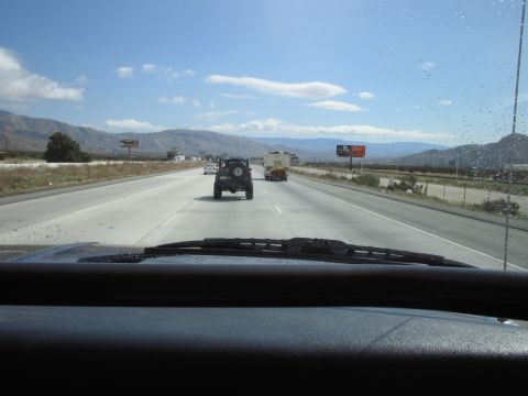 1985 Ford Bronco - Rear view of a black SUV with a spare tire mounted on the back, traveling on a highway with mountains in the distance.