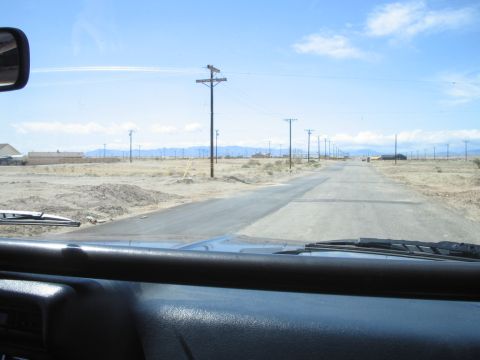 1985 Ford Bronco - View from inside a vehicle traveling on a desolate road through a dry, open area under a bright blue sky.
