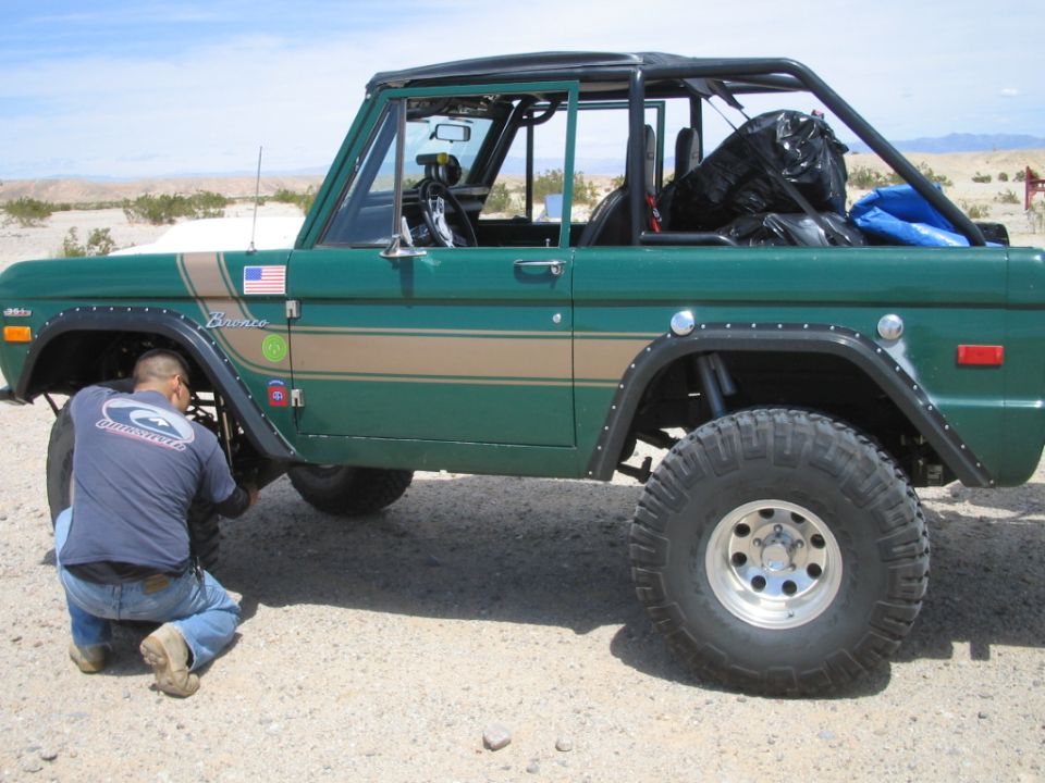 Green Ford Bronco in profile with person working on front axle in the desert.