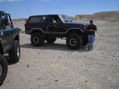 1985 Ford Bronco - A black Ford Bronco is parked in a desert landscape next to another off-road vehicle.