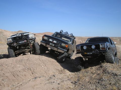 1985 Ford Bronco - Three modified SUVs tackle an off-road trail, with one appearing to be a Ford Bronco.
