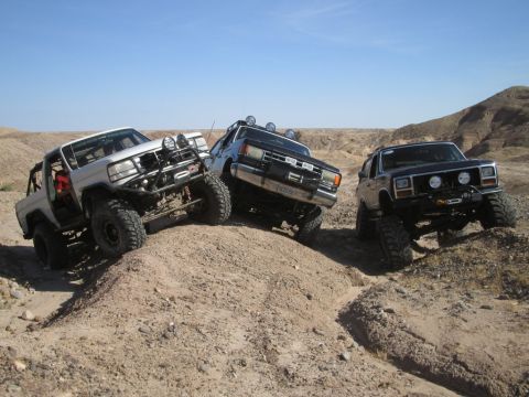 1985 Ford Bronco - Several off-road vehicles navigate a challenging desert terrain under a clear blue sky.