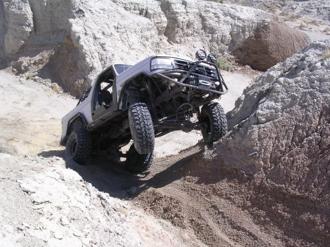 1985 Ford Bronco - Modified SUV navigates a steep, rocky trail in a desert landscape.