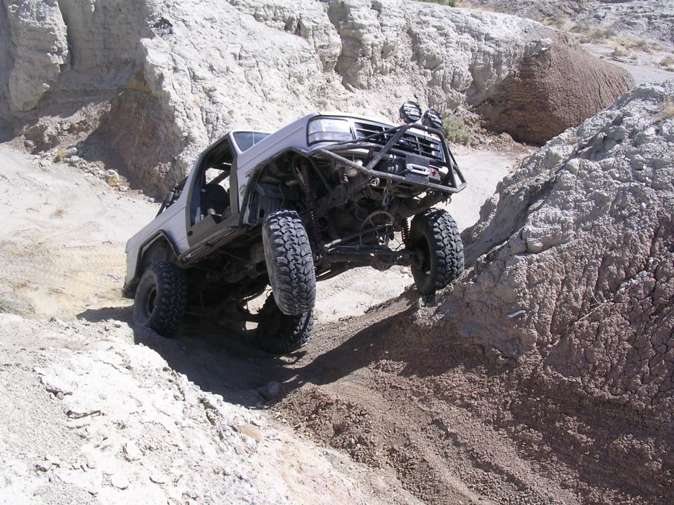 White tube-frame Bronco with big tires climbing rocks in desert