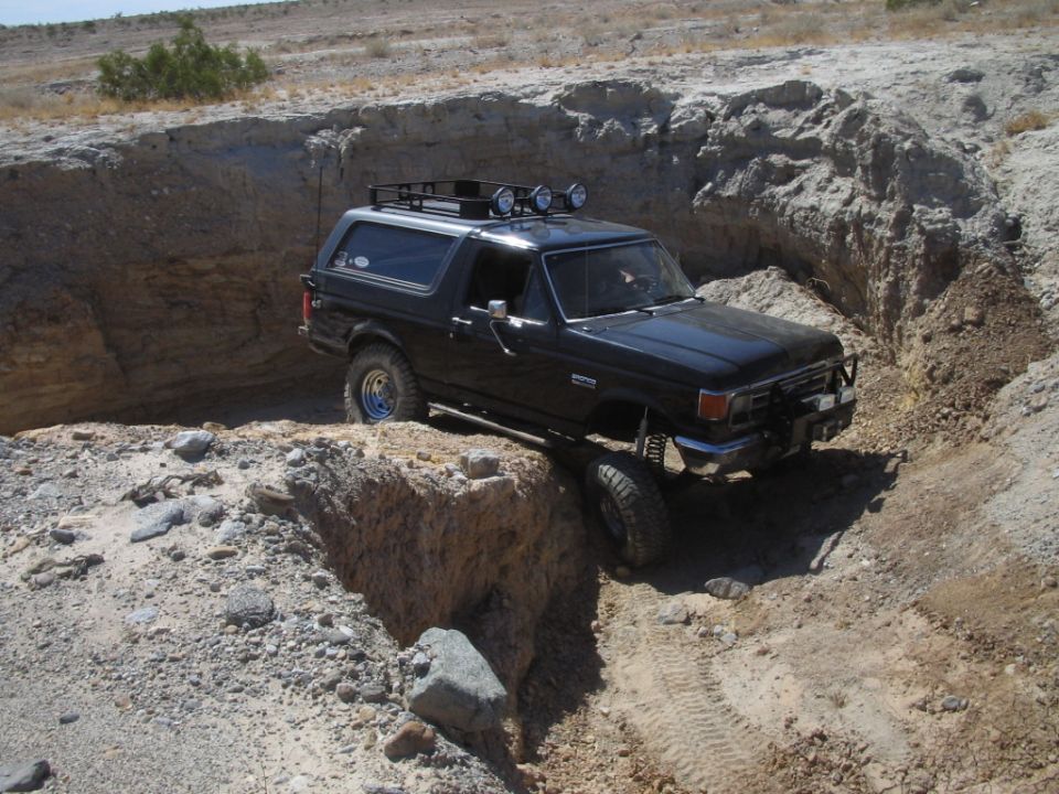 Black Ford Bronco climbing rocky desert ravine with roof rack and light bar