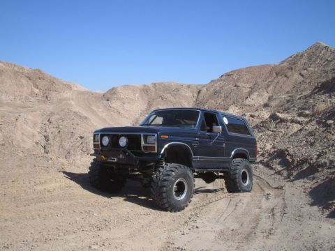 1985 Ford Bronco - This lifted SUV navigates a desert trail, its large tires and modified suspension ready for off-road adventure.