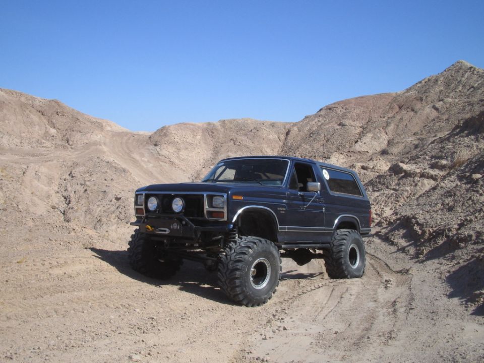 Dark blue lifted Ford Bronco with big mud tires on desert trail