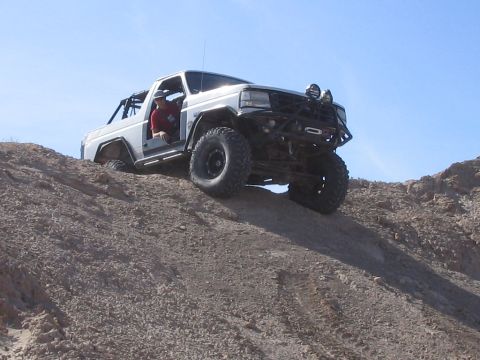 1985 Ford Bronco - Modified 1985 Ford Bronco tackling a challenging off-road climb under a clear blue sky.