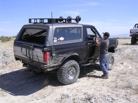 1985 Ford Bronco - A man stands by the open driver's door of a modified Ford Bronco in a desert landscape.