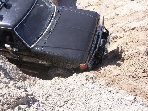 1985 Ford Bronco - A black 1985 Ford Bronco navigates a challenging off-road terrain, getting stuck in a deep dirt ditch.