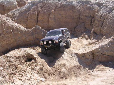 1985 Ford Bronco - Modified 1985 Ford Bronco navigates a challenging off-road course with large tires and lifted suspension.