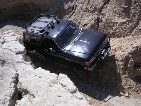 1985 Ford Bronco - A black Ford Bronco is shown driving through a tight, rocky off-road trail.