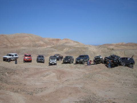 1985 Ford Bronco - A group of SUVs and trucks are gathered in a desert environment under a clear blue sky.