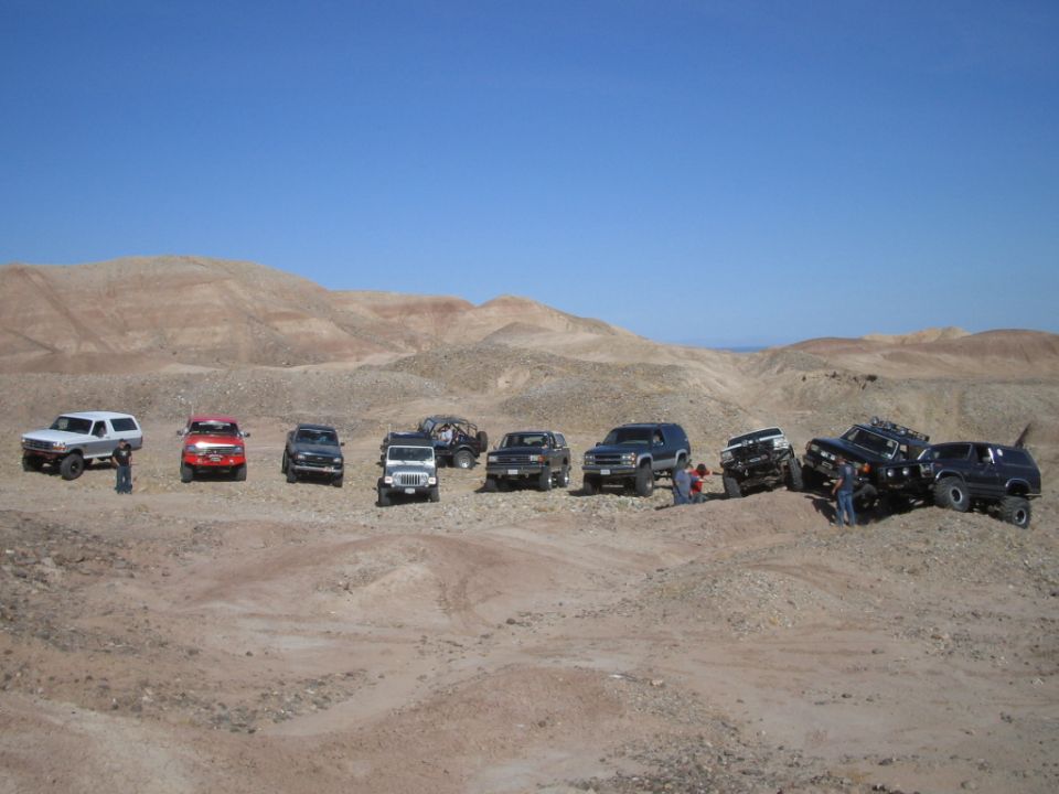 Row of lifted 4x4 SUVs and trucks parked in a desert off-road area