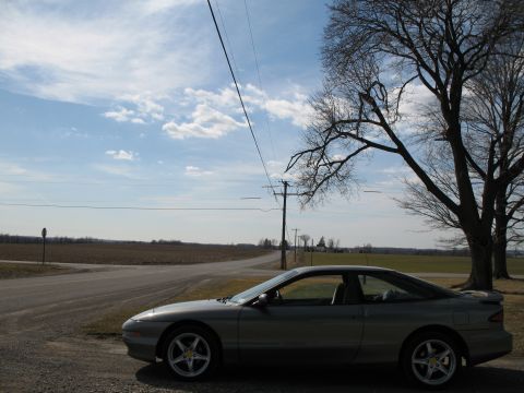 1996 Ford Probe - A silver 1996 Ford Probe coupe is parked on a gravel shoulder next to a rural road.