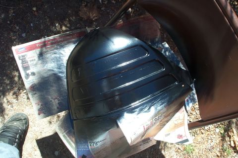 1999 Ford Crown Victoria - A black car part is being painted and placed on top of newspapers.