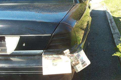 1999 Ford Crown Victoria - The rear of a black car shows modified taillights covered partially by newspaper, with a "Supermotors.net" watermark visible.
