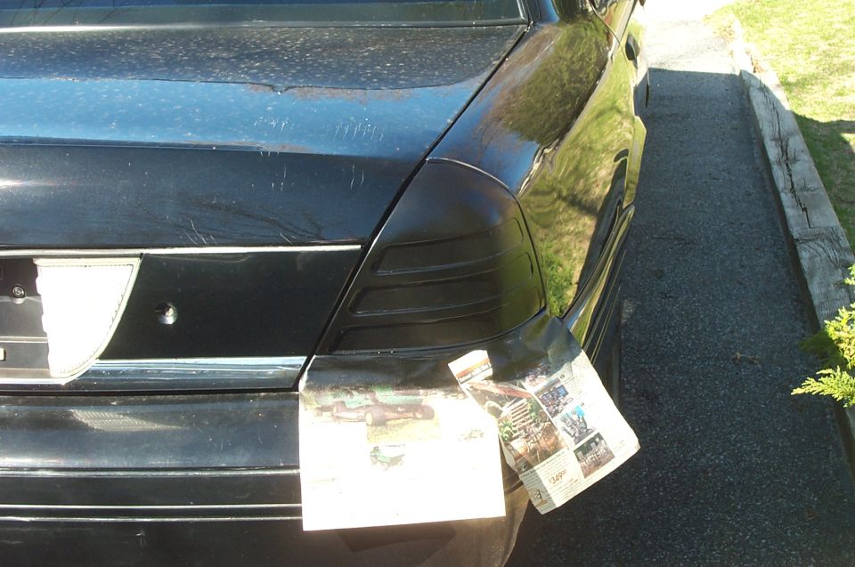 Blacked-out painted taillight on rear corner of black Crown Victoria, newspaper masking taped below