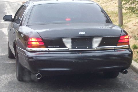 1999 Ford Crown Victoria - Rear view of a black sedan with Crown Victoria badging and dual exhaust pipes.
