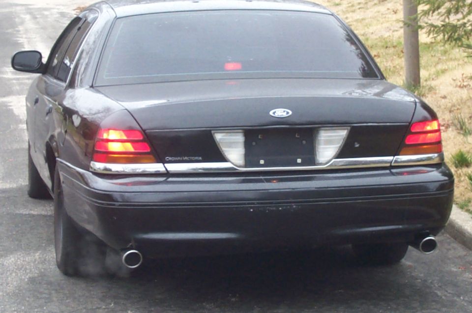 Rear view of black Ford Crown Victoria with dual chrome exhaust tips, lights on