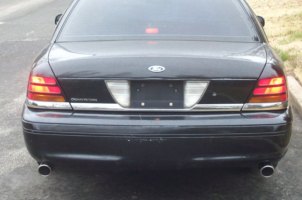 Straight-on rear of wet black Ford Crown Victoria with lights on and dual chrome exhaust tips