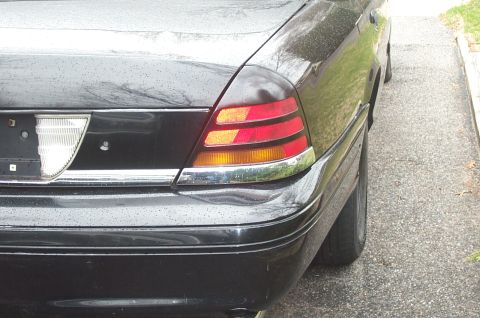 1999 Ford Crown Victoria - Close-up of the right rear corner of a black Crown Victoria sedan, showing the striped red-and-amber taillight lens with chrome surround, c…