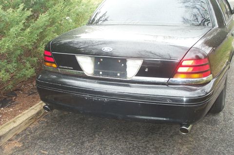 1999 Ford Crown Victoria - The rear of a black Ford Crown Victoria is shown parked next to some bushes.