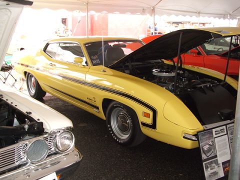 1966 Ford Ranchero - A yellow 1970 Ford Torino GT coupe, black racing stripes and an open hood, is displayed next to a white vehicle.