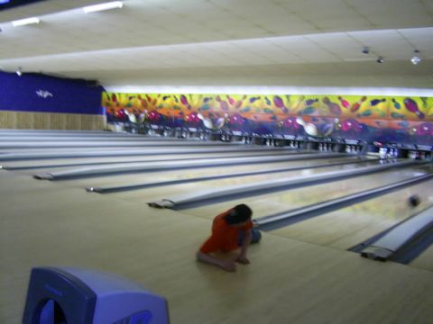 1985 Ford Bronco - A person sits on the floor of a bowling alley next to a bowling ball, with lanes stretching into the distance.