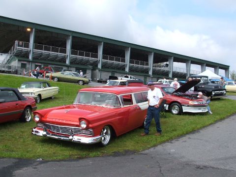 1966 Ford Ranchero - A red and white 1957 Ford Fairlane station wagon is parked on grass with other vehicles and a grandstand in the background.