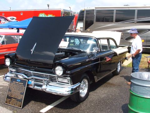 1966 Ford Ranchero - A black 1957 Ford Custom is displayed with its hood open, parked beside a large RV at an outdoor event.