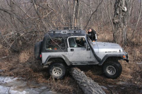 1995 Jeep Cherokee - A person is looking at a silver Jeep Wrangler TJ that is stuck on a log in a wooded area.