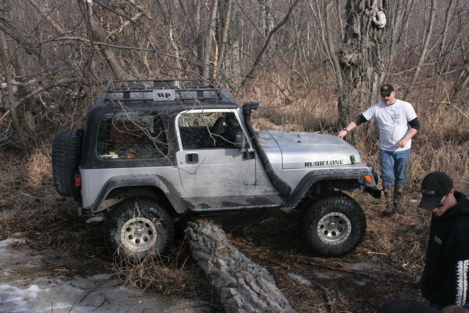 Silver Jeep Wrangler Rubicon with a roof rack and snorkel, parked off-road with a man standing beside it