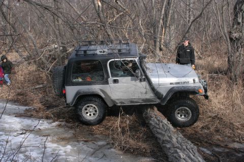 1995 Jeep Cherokee - A silver Jeep Wrangler Rubicon is shown off-roading through a wooded area with a snorkel and roof rack.
