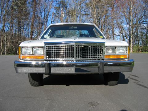 1985 Ford LTD Crown Victoria - The front of a white sedan is shown, a large chrome grille and prominent bumper.