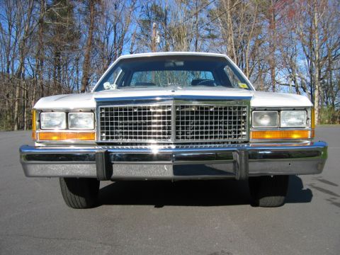1985 Ford LTD Crown Victoria - Frontal view of a white 1980s Ford sedan with a prominent chrome grille and bumper.
