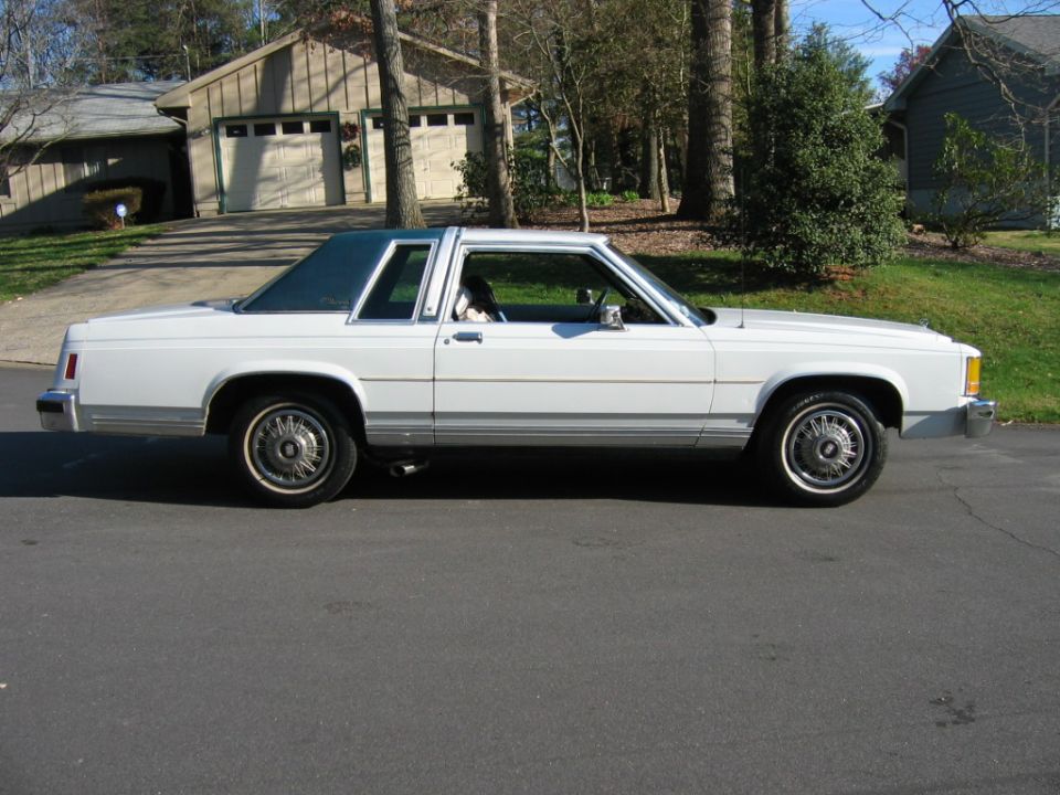 White two-door sedan parked on a residential street, side view