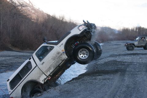 1995 Jeep Cherokee - An off-road pickup truck is stuck in a ditch while another vehicle watches.
