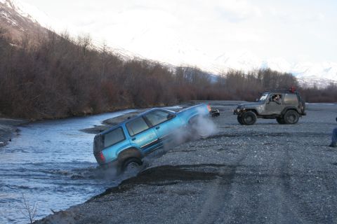 1995 Jeep Cherokee - Two SUVs navigate a rough, watery terrain with snow-capped mountains in the background.